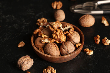 Wooden bowl with tasty walnuts and nutcracker on black background
