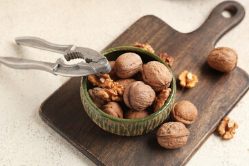 Bowl with tasty walnuts and nutcracker on white background