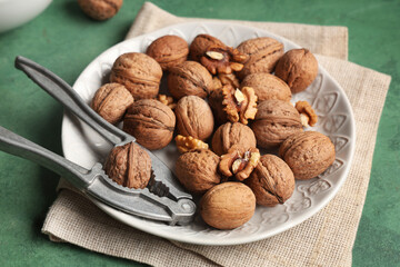 Plate with tasty walnuts and nutcracker on green background