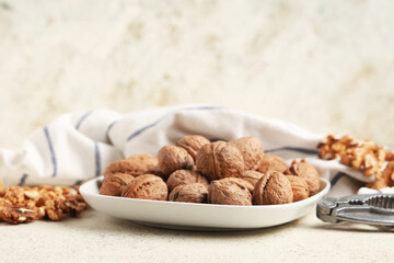 Plate with tasty walnuts and nutcracker on white background