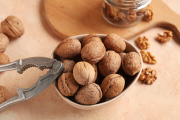 Bowl with tasty walnuts and nutcracker on beige background