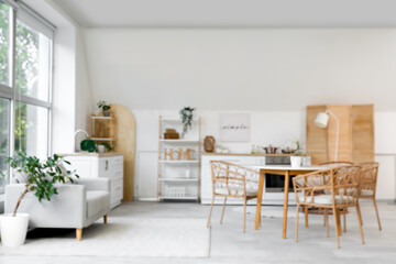 Blurred view of light kitchen with counters, sofa and dining table