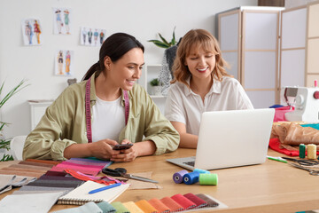 Obraz premium Female tailors working with laptop at table in atelier