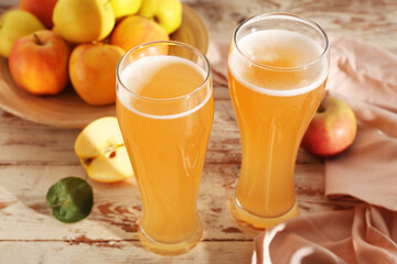 Glasses of fresh apple kvass and plate with fruits on white wooden background