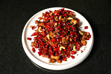 Bawang Spicy Chicken or Stir fried Chicken Cubes with Red Chili, sesame seeds and cashew nuts with chopsticks served in dish on dark background top view of hong kong food