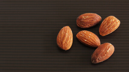 Roasted almond nuts group on black and brown striped background
