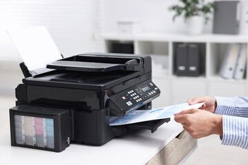 Woman using modern printer at workplace indoors, closeup