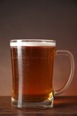 Mug with fresh beer on wooden table against brown background, closeup