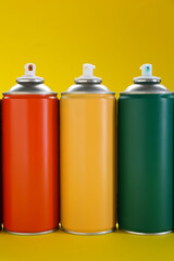 Three spray paint cans on yellow background