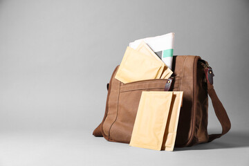 Brown postman's bag with envelopes and newspapers on grey background. Space for text