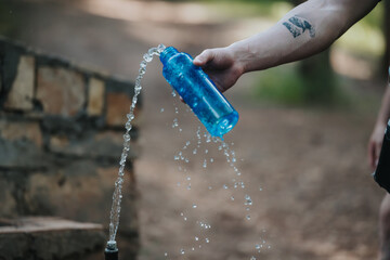 A close-up of water being poured from a blue bottle outdoors, evoking a sense of refreshment and...
