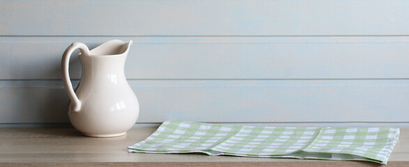 kitchen banner, a table in front of a white board wall and a jug. a green checkered towel on the countertop.