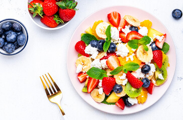 Fruity summer salad with fresh berries, ricotta cheese, banana, kiwi and mint, white background, top view