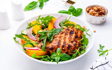Fresh healthy eatung salad with peaches, chicken, cucumber, nuts, onion, basil and arugala, white background, top view