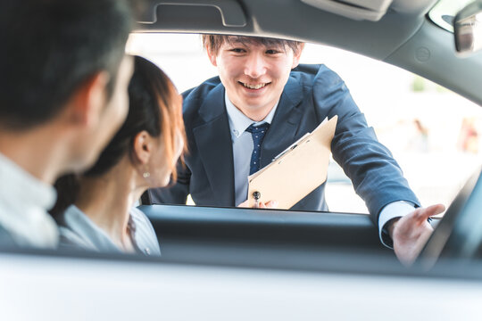 自動車購入・査定・買取にきた顧客を接客するセールスマンの若いアジア人男性
