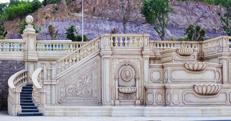 A monumental staircase constructed in a classic Baroque style. The staircase is adorned with elaborate balustrades featuring intricate floral motifs and sculptures. 