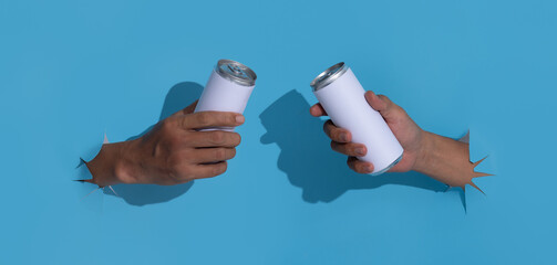 Male hand with tin can breaks through blue paper background.