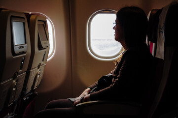 Woman on an international flight sitting in an airplane seat by the window.