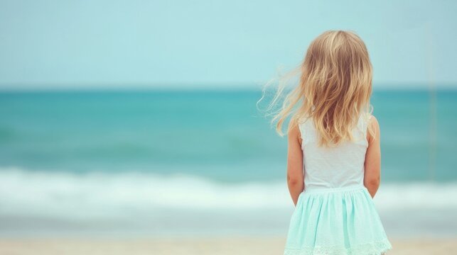 A little girl stands on the beach, waving an American flag as she enjoys the sunny day by the ocean. - Powered by Adobe