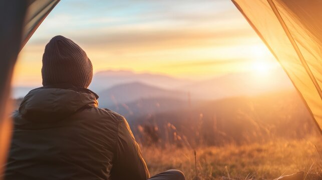 A man relaxes in his tent, taking in the breathtaking mountain landscape as the sun rises.