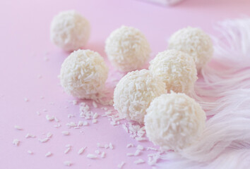 Top view of White Chocolate Candy With Coconut Topping On White Feather and pink background, sweet balls on plate flat lay with copy space. Romantic gift for celebration or anniversary