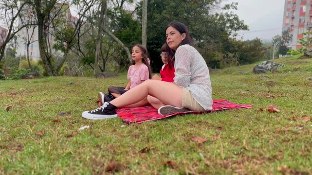 International Children Day. Latin mother having fun with her young children outdoors. Sitting on the ground playing with their hands. Concept of family. Single mother with two young children.
