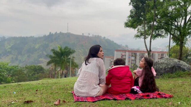 International Children Day. Latin mother having fun with her young children outdoors. Sitting on the ground playing with their hands. Concept of family. Single mother with two young children.