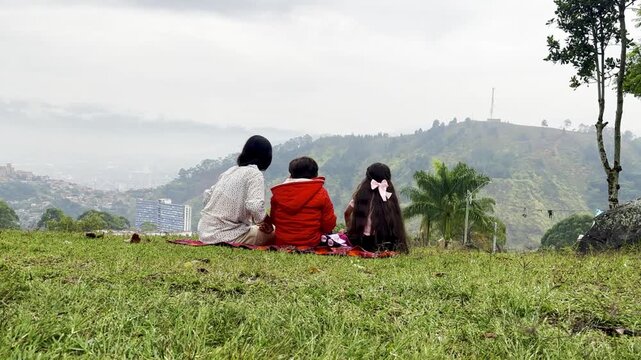 International Children Day. Latin mother having fun with her young children outdoors. Sitting on the ground playing with their hands. Concept of family. Single mother with two young children.