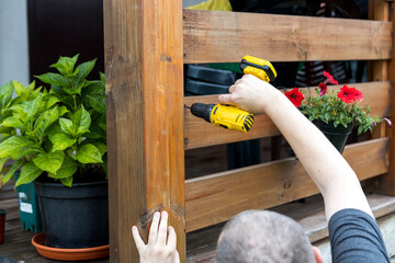A man is using a drill to attach a wooden post to a fence