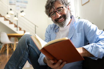 Fototapeta na wymiar Happy mature man with glasses relaxing at home reading a book.