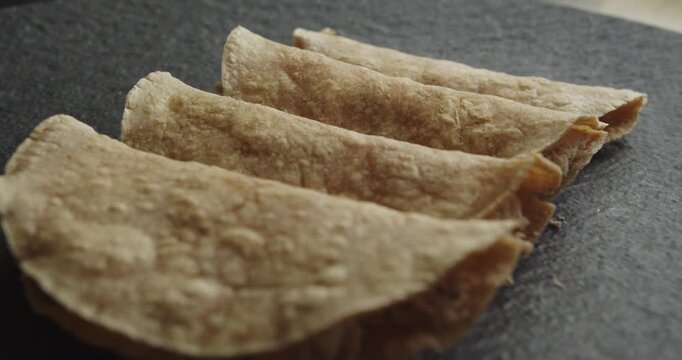 Beautiful slow motion close-up shot with slight movement of a group of chicken chilaquiles tacos or tortillas on a black plate in a dimly lit industrial kitchen.