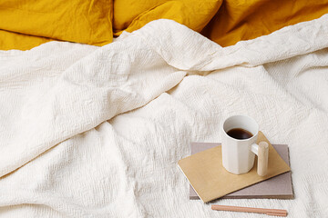 Cozy bed with yellow pillows, notebook, pen and coffee mug.