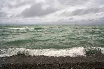 An incoming wave on the Black Sea and a pebble beach on the Sochi coast on a summer day with clouds, Sochi, Krasnodar Territory, Russia