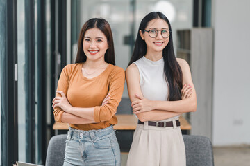 Two confident Asian businesswomen stand with crossed arms in office.