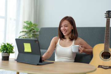 Beautiful young Asian woman smiling Work using laptop and drink coffee in living room at home. Asian business woman working in finance and using mobile phone to enjoy time relaxing.