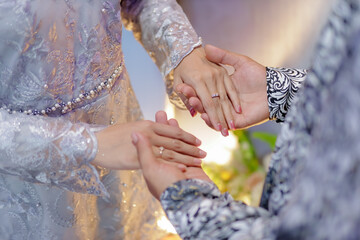 A pair of hands holding each other, wearing engagement rings and kebaya dresses. Boyfriend proposing to his girlfriend to get married. Concept of people relationship, ring present and love