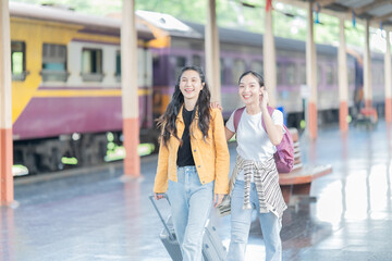 two young Asian woman is walking with suitcase at railway stations, using the smartphone and map, traveling by train.