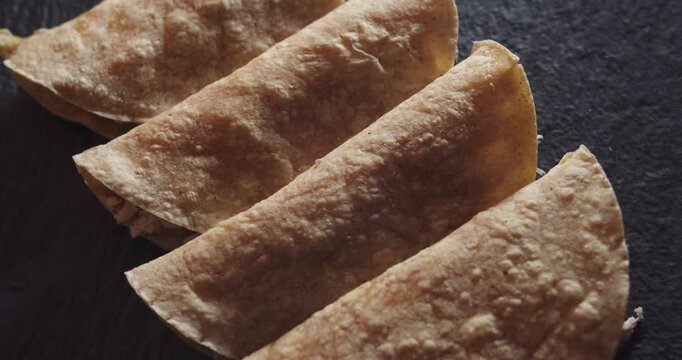 Beautiful slow motion shot of a group of 4 tacos or Mexican tortillas with chicken placed on a black plate and dimly lit. It is a close-up with smooth and continuous movement on the tortillas.