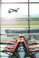 Passenger plane taking off and waiting room in the background. Lounge with track view. Empty seats © Burak