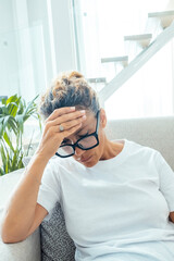 Unhealthy mature woman sitting on couch at home closed eyes touch head feels overheated, aged...