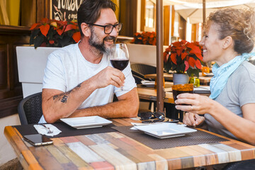 Adult happy couple enjoy restaurant lunch together clinking and toasting red wine sitting at the table. Mature people man and woman in summer holiday leisure vacation eating and drinking. Dating day
