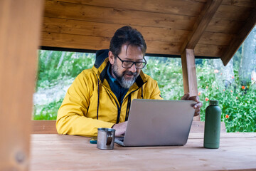 Online working adult travel influencer freelance sitting in a wooden cabin in the forest. Modern business and roaming connection technology concept people. Alternative office workplace adult male