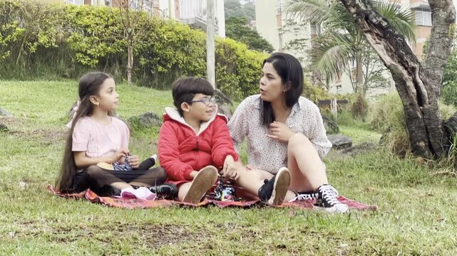 International Children Day. Latin mother having fun with her young children outdoors. Sitting on the ground playing with their hands. Concept of family. Single mother with two young children.