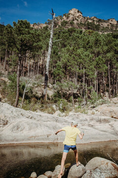 Boy jumping on rocks in a Corsican river with a forest backdrop
