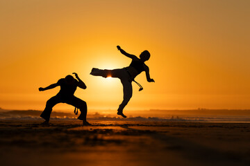 Two people are practicing karate on a beach at sunset