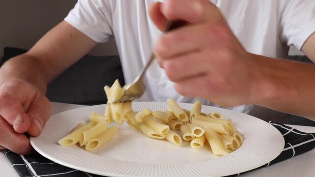 A man impales feather pasta on a fork as he eats.