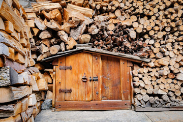 Pontechianle, Italy. Wooden logs stacked on the wall of a mountain house. Miniature wooden house for storing tools.