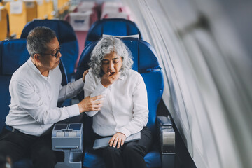 A mature woman sits by the window on a passenger plane, traveling abroad. She looks unwell, experiencing a headache, nausea, and vomiting, which dampens her travel excitement.