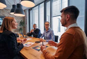 In the vibrant ambiance of a modern startup office, a diverse team of business professionals engage in discussions on various projects and develop new business strategies, epitomizing creativity and