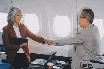 business people at meeting in private plane, Asian businessman in suit is talking to woman in jet and pointing at blank laptop screen, colleagues are discussing deal and flying in plane